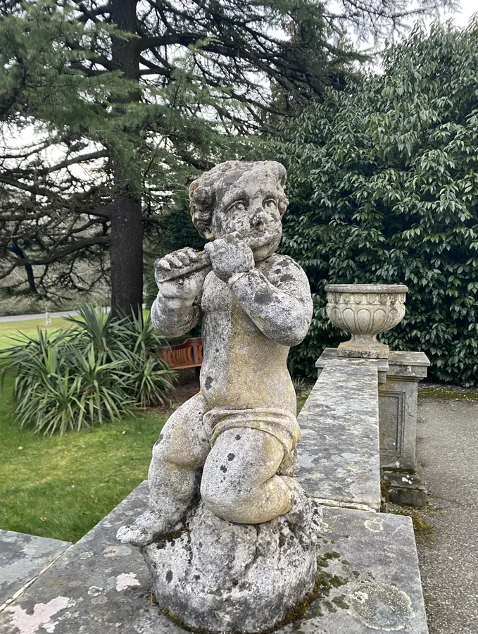 Weathered stone cherub statue playing a flute in a garden