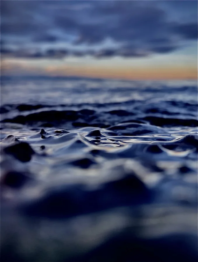 Ocean waves seen at water level beneath a pastel sunset