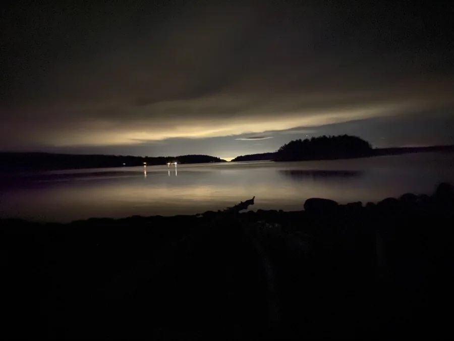 Calm lake at night with distant lights under low clouds