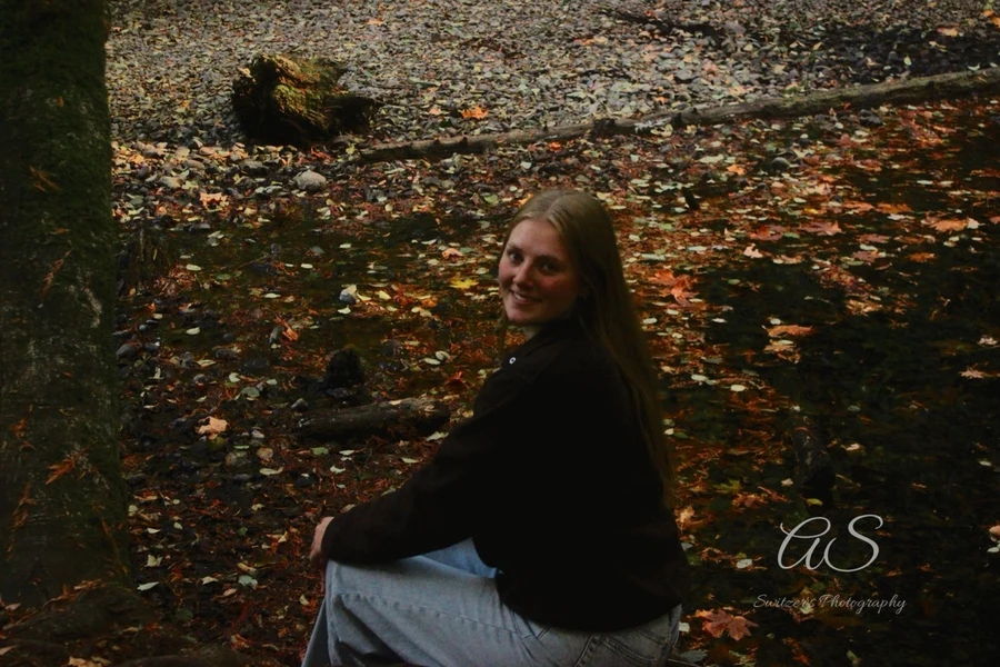 Young woman sitting among fallen autumn leaves beside a creek