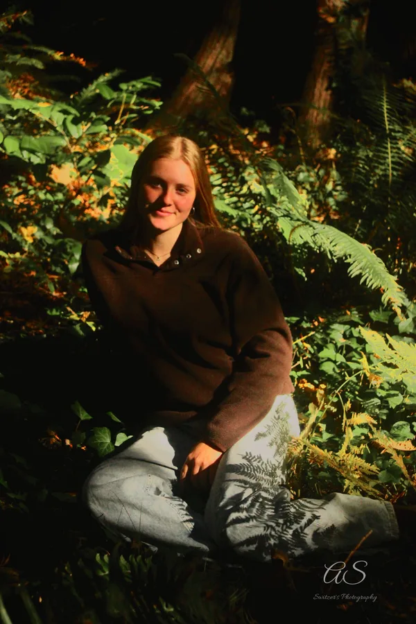 Young woman smiling among sun-dappled ferns