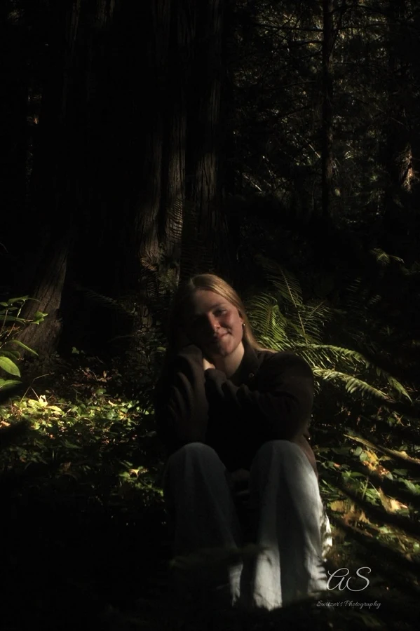 Young woman sitting in deep forest shade among ferns
