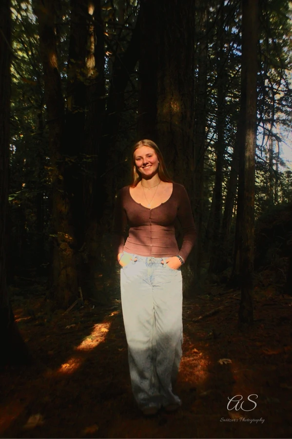 Young woman standing in a sun-dappled forest with hands in her pockets